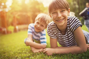 Little boy aged 5 and his elder sister aged 9 are having fun laughing on the garden lawn grass.